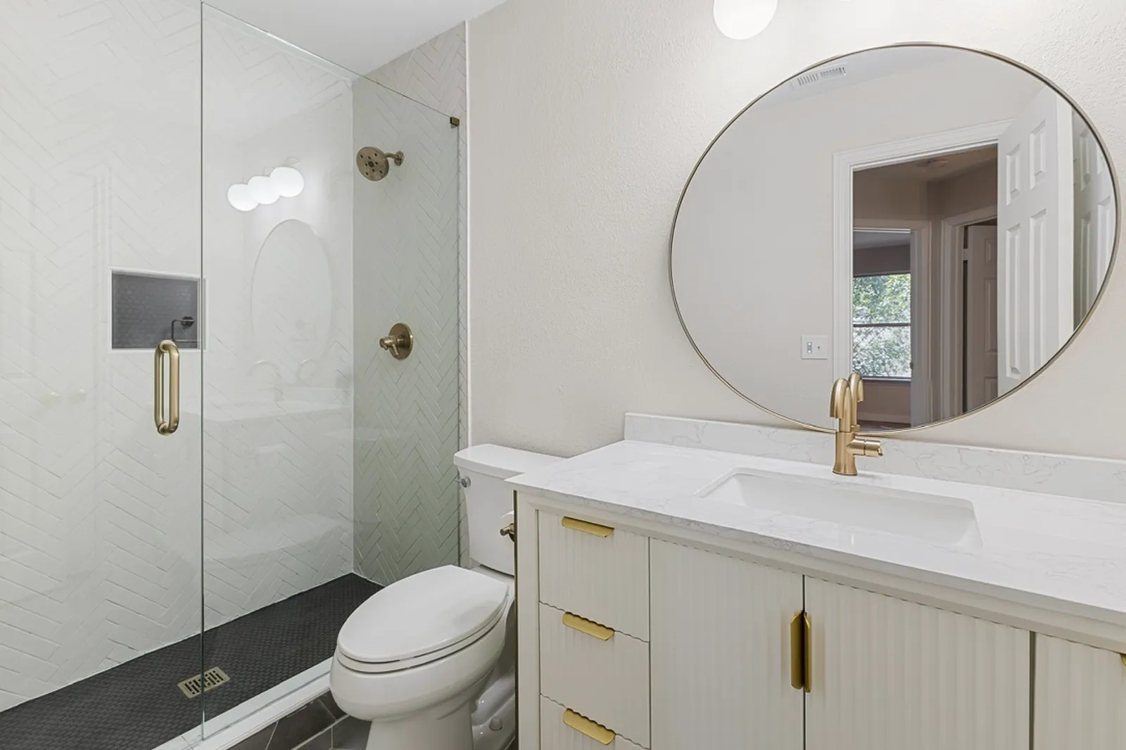 Second bathroom at Azure Ln. in Addison: glass shower, round mirror, and fluted vanity