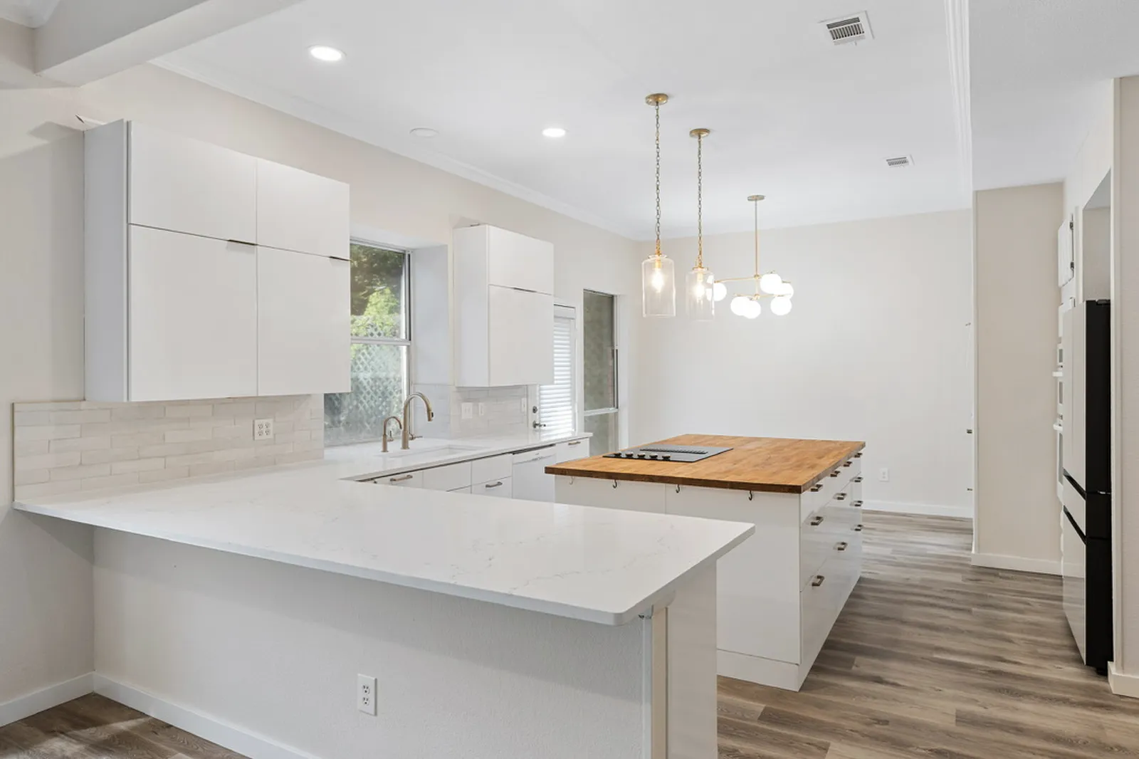 Kitchen at Azure Ln. in Addison after the renovation: white cabinets, white quartz counters, wood-top island, and pendant lights
