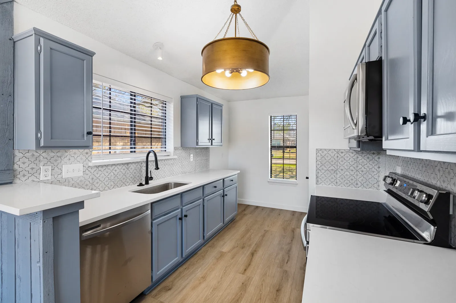 Kitchen after a pre-sale renovation by Renovation Sells Dallas at Haven Pl in Allen, TX: painted blue-gray cabinets, white quartz counters, brass pendant, and new flooring