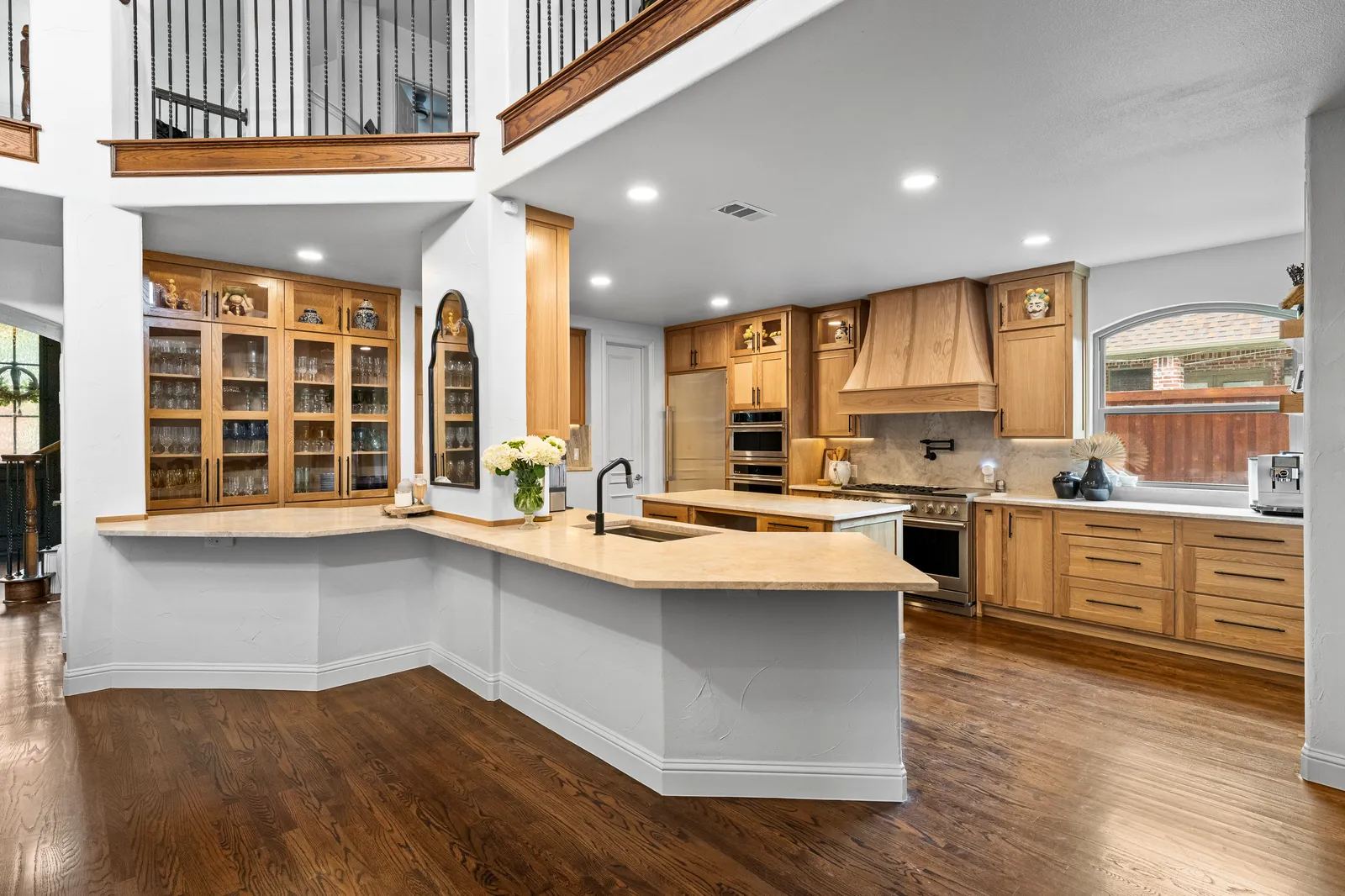 Remodeled kitchen at Shady Point Dr in Plano, TX by Renovation Sells Dallas: white oak cabinetry, plaster range hood, quartz island, and refinished hardwood floors